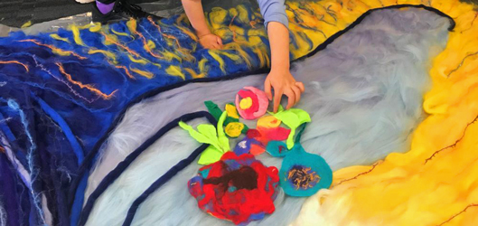large felt artwork in progress student hands placing felt flowers